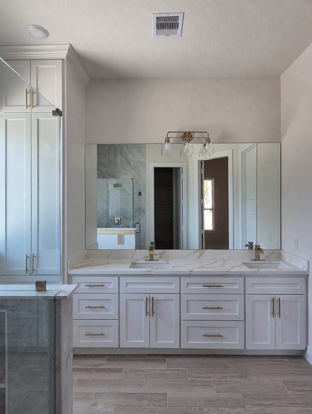 Bathroom double vanity remodel with white cabinetry, gold fixtures, and a large mirror