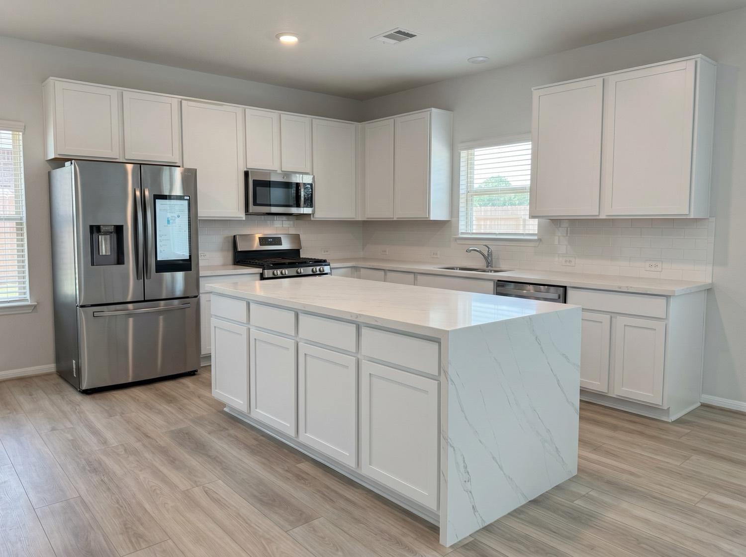 Kitchen remodel with waterfall quartz island, white cabinetry, and stainless steel appliances